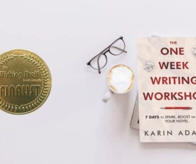 A copy of The One Week Writing Workshop Book by Karin Adams rests beside a latte, a pair of glasses, and a gold-coloured medal proclaiming the book to be a finalist in The Wishing Shelf Book Awards
