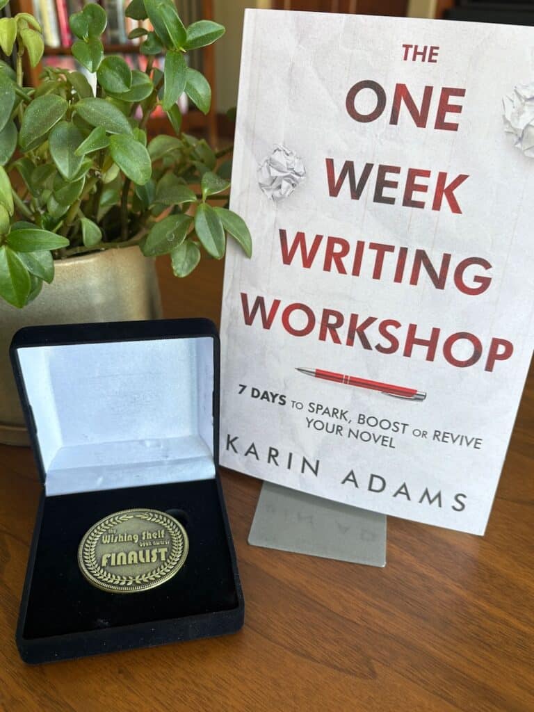 a photo of Karin Adams' book The One Week Writing Workshop beside a plant and a Finalist medal in a box from the Wishing Shelf Book Awards